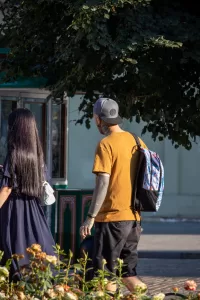 Фото тату на руках и шее мужчины, идущего по улице. Видны детализированные рисунки в стиле традишнл.