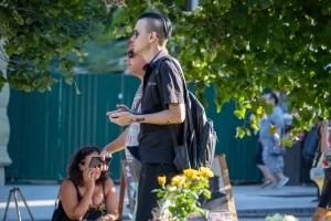 Фото тату: мужчина с татуировкой кота на предплечье, держащий в руке телефон. Фотография сделана на улице при дневном свете.