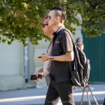 Фото тату: черно-серый рисунок кота, окруженного цветами, на руке мужчины. Детализированный эскиз тату с использованием теней и градиентов.