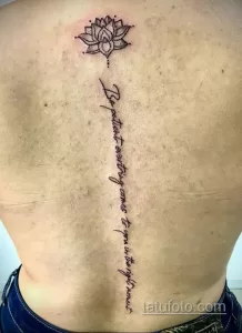 Фото тату: Черно-серая татуировка лотоса на спине с вертикальной надписью 'Be patient everything comes to you in the right moment'.