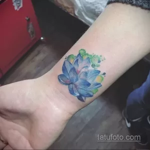 Фото тату: акварельный лотос на запястье с добавлением зеленых и желтых брызг краски. Нежный и оригинальный рисунок татуировки.
