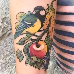 Фото тату синицы, сидящей на ветке с яблоком и цветами, выполненное в ярких осенних тонах. Красивый рисунок татуировки.