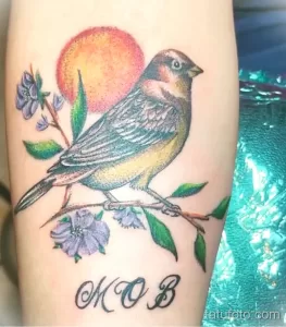 Цветная татуировка птицы на ветке с цветами и надписью 'MOB'. Яркие цвета и детализированный рисунок.