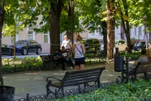 Фотография с улицы, на которой девушка с татуировкой на спине идет по парку. Татуировка представляет собой цветочный узор в черных тонах.