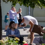Фото мужчины с татуировкой на руке, смотрящего вниз, и женщины на улице. Видна часть рисунка татуировки в виде темных линий. Уличная фотография тату.