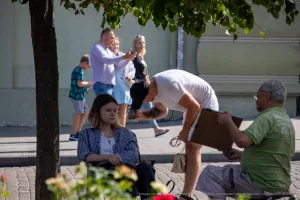 Фото мужчины с татуировкой на руке, смотрящего вниз, и женщины на улице. Видна часть рисунка татуировки в виде темных линий. Уличная фотография тату.