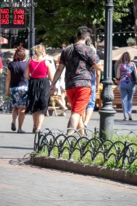 Фото мужчины с татуировкой на руке, идущего по улице с розовой сумкой и разговаривающего по телефону. Татуировка изображает тропические листья.