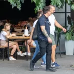 Фотография мужчины с татуировкой на предплечье, идущего по улице. Татуировка выполнена в ярких цветах и изображает череп с цветами.