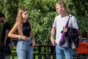 Фотография молодого человека с татуировками на руках и шее, стоящего на улице. Современный стиль, городская обстановка, повседневная одежда.