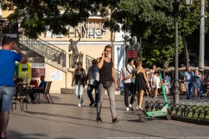 Фото тату на руке мужчины: небольшой рисунок, расположенный на предплечье. Мужчина разговаривает по телефону на фоне городской архитектуры.