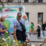 Фотография мужчины с татуировками на плече и кепкой, стоящего рядом с фургоном с мороженым. Акцент на повседневном стиле и летней атмосфере.
