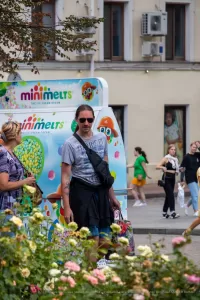 Фотография мужчины с татуировками на плече и кепкой, стоящего рядом с фургоном с мороженым. Акцент на повседневном стиле и летней атмосфере.