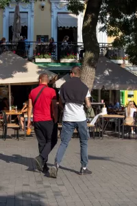 Фотография мужчины с татуировкой на руке, идущего по улице города. Татуировка выполнена в темных тонах и видна на предплечье.