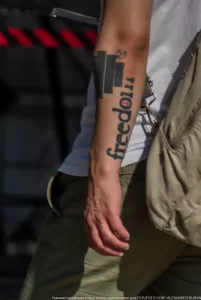 Фотография татуировки с надписью "Freedom" и изображением здания на руке мужчины. Татуировка выполнена в черном цвете.