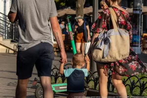 Фото тату на руке мужчины, идущего с семьей по улице. Татуировка выполнена черными чернилами в виде иероглифов.