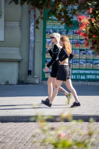 Фотография молодой девушки, идущей по улице с видимыми татуировками на лодыжках и икрах. Девушка одета в черную футболку и шорты.