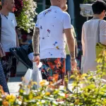 Фото татуировок на руках мужчины с бородой в яркой летней одежде. Рукава украшены разноцветными брызгами краски и абстрактными рисунками.