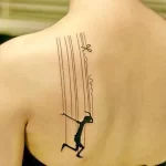 Фото минималистичной татуировки на спине с изображением марионетки. Тонкие линии и лаконичный дизайн.