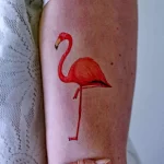 Фото тату минималистичного фламинго на предплечье. Изящный рисунок в красных тонах, простой и элегантный эскиз татуировки.