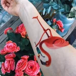 Фото оригинальной татуировки фламинго на предплечье, выполненной в ярких тонах с добавлением геометрических элементов и абстрактных фигур.