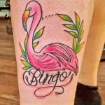 Фото классической татуировки фламинго с надписью 'Bingo'. Яркие цвета, четкие контуры, традиционный стиль. Оригинальный и запоминающийся рисунок.