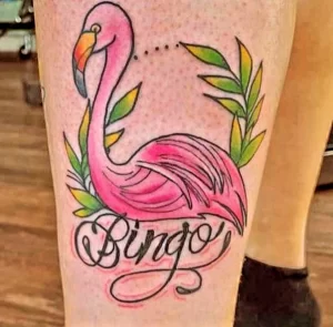 Фото классической татуировки фламинго с надписью 'Bingo'. Яркие цвета, четкие контуры, традиционный стиль. Оригинальный и запоминающийся рисунок.