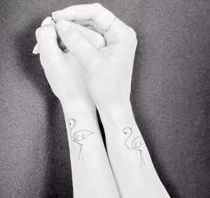 Фото тату: два минималистичных рисунка фламинго на запястьях. Изображения выполнены тонкими линиями, символизируя связь и единство.