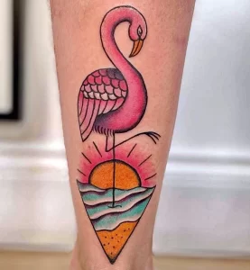 Фото минималистичной татуировки на икре, изображающей розового фламинго на фоне заката с морем и солнцем. Простые линии и яркие цвета.