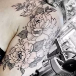 Фото тату пышных цветов, выполненных в технике black and grey на плече. Детализированный рисунок татуировки с акцентом на лепестки и листья.