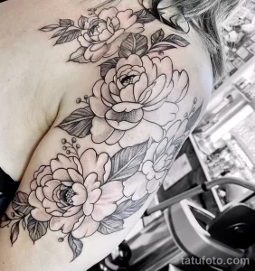 Фото тату пышных цветов, выполненных в технике black and grey на плече. Детализированный рисунок татуировки с акцентом на лепестки и листья.