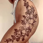 Фото тату изящных цветов, выполненных в технике line work на женском бедре. Детализированный рисунок татуировки с акцентом на лепестки и листья.