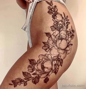 Фото тату изящных цветов, выполненных в технике line work на женском бедре. Детализированный рисунок татуировки с акцентом на лепестки и листья.