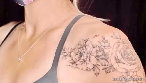 Фото татуировки на плече с изображением цветущих пионов и роз. Рисунок выполнен в черно-белой гамме с использованием тонких линий и точек.