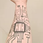 Фото тату на предплечье, изображающее сложную систему микросхем и электронных дорожек. Черно-белый рисунок татуировки в стиле киберпанк.