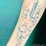 Фото тату: минималистичное изображение лица, выполненное в геометрическом стиле с использованием синих оттенков. Татуировка расположена на руке.
