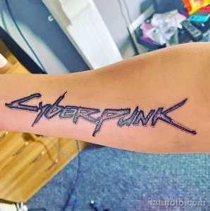 Фото тату на руке: минималистичная надпись 'Cyberpunk', выполненная в черном цвете с использованием тонких линий и точечной техники.