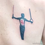 Фото тату с изображением гимнаста, выполняющего упражнение на перекладине. Силуэт выполнен в темно-синем цвете на светлой коже.