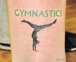 Фото тату гимнастки в прыжке с надписью 'GYMNASTICS'. Черно-серые тона, реалистичный стиль, расположение на руке.