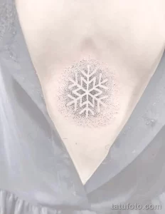 Фото тату: снежинка, выполненная точками (dotwork) на груди. Изящный и минималистичный рисунок татуировки с использованием техники точечной штриховки.