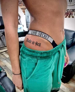 Фото татуировки надписью 'Love Secret Made in Hell' на талии девушки. Черно-белая татуировка, выполненная простым шрифтом. Идея для тату.