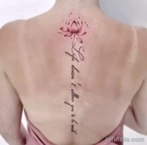 Фотография татуировки на спине с изображением цветка лотоса и вдохновляющей надписи, выполненной в минималистичном стиле.