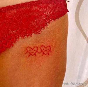 Фото тату: небольшая татуировка двух стилизованных сердец, выполненная тонкими линиями на животе девушки. Нежный и романтичный рисунок татуировки.