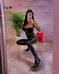 Фотография девушки в черной одежде с детальной татуировкой на руке, демонстрирующая современный стиль и искусство татуировки.