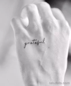 Фото тату: надпись "grateful" (благодарный) изящным шрифтом расположена на стопе. Эскиз татуировки, минимализм, каллиграфия.