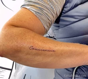 Фото тату: надпись "Consciencia" (сознание) изящным шрифтом на предплечье. Минималистичная татуировка, напоминающая о важности осознанности.