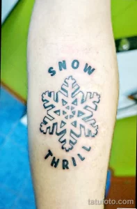 Фото татуировки снежинки с надписью 'SNOW THRILL' на руке. Оригинальное сочетание рисунка и текста, передающее любовь к зимним развлечениям.