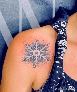 Фото тату: большая снежинка, выполненная точками (dotwork), на плече. Изящный рисунок татуировки в технике pointillism, создающий эффект воздушности и легкости.