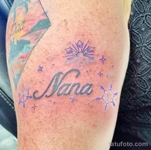 Фото тату имени 'Nana', выполненного красивым шрифтом, украшенного снежинками и звездами. Рисунок расположен на руке.