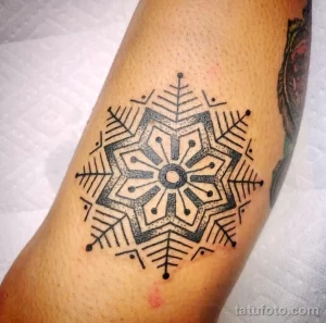 Фото тату геометрической снежинки на руке. Черно-белый рисунок татуировки в стиле дотворк с тонкими линиями и точками.