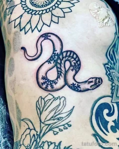 Фото тату змеи, обвитой снежинками на руке. Черно-белая гамма, детализированный рисунок, оригинальный дизайн. Символичное и эффектное изображение.